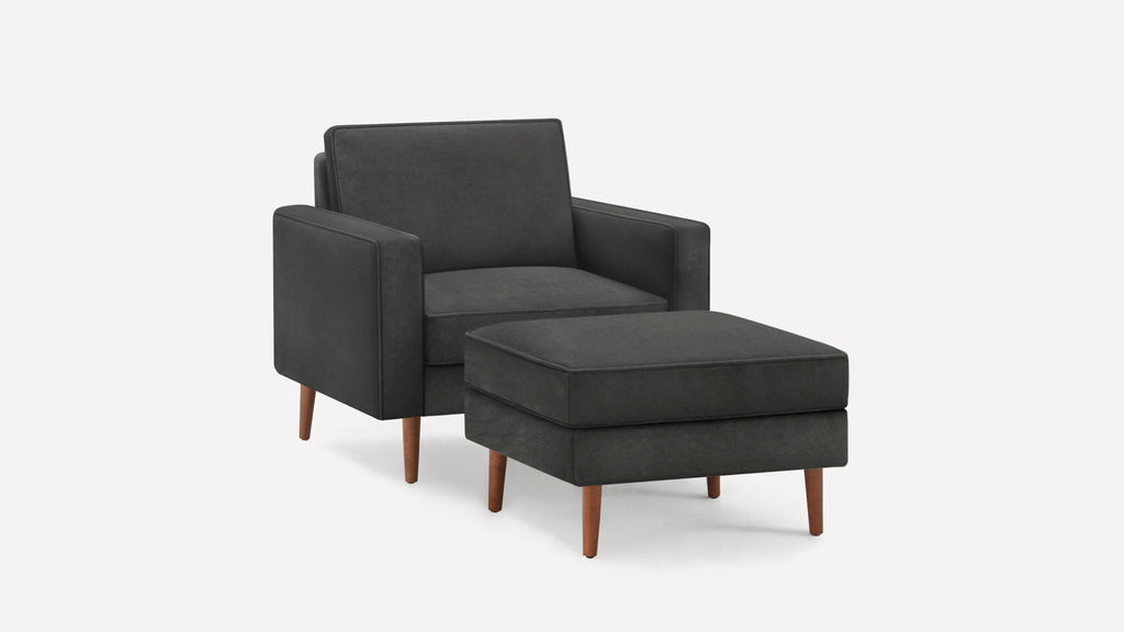Dark gray upholstered armchair with matching ottoman, featuring wooden tapered legs and a modern, minimalist design.