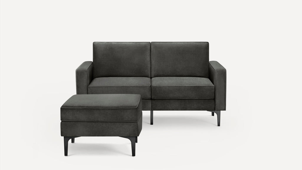 Dark gray modern sofa with matching upholstered ottoman, featuring clean lines and black metal legs on a white background.