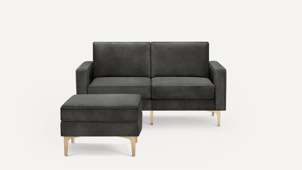 Dark gray modern loveseat sofa with matching ottoman, featuring sleek gold metal legs and clean lines on a white background.