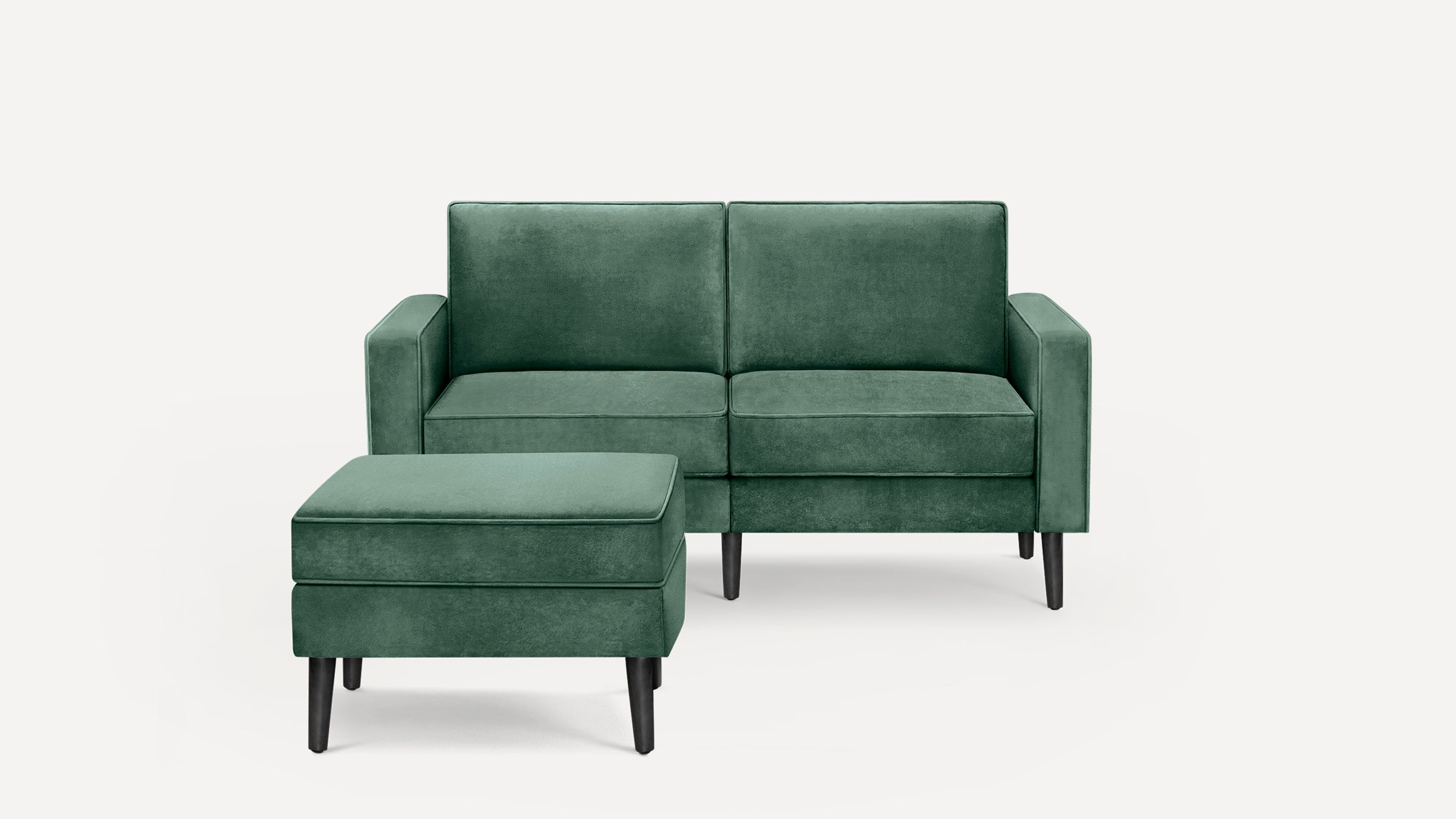 Green velvet two-seater sofa with matching ottoman, featuring clean lines and dark wooden legs on a white background.