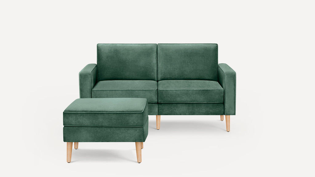 Green velvet two-seater sofa with matching ottoman, featuring wooden legs and clean, modern lines against a white background.
