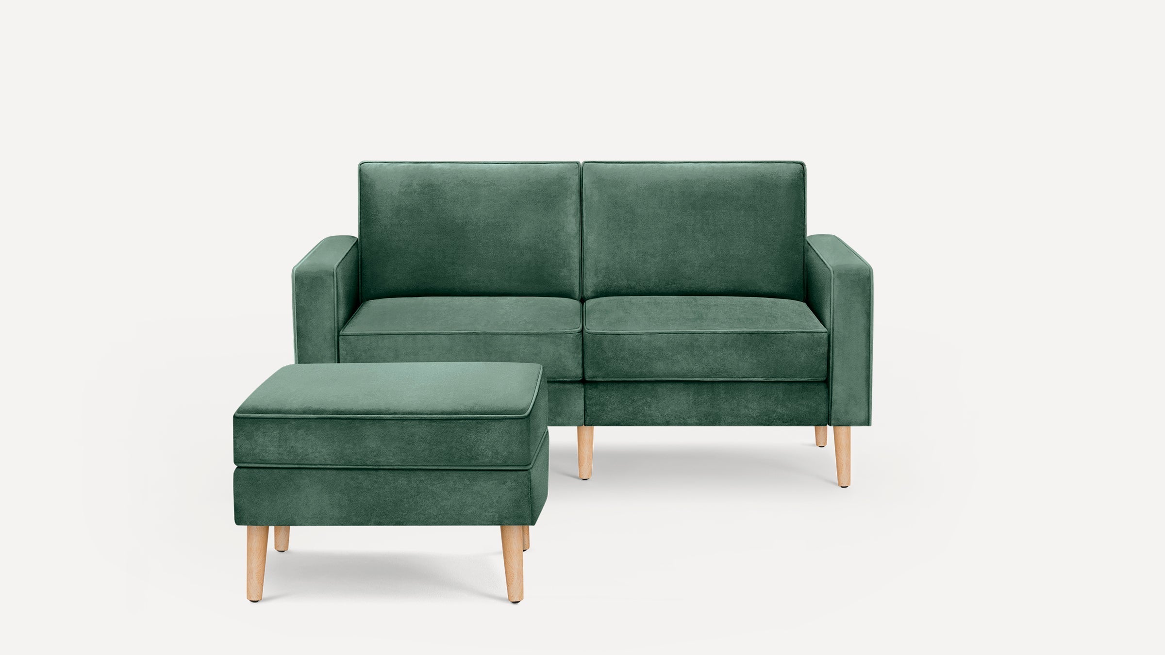 Green velvet two-seater sofa with matching ottoman, featuring wooden legs and clean, modern lines against a white background.