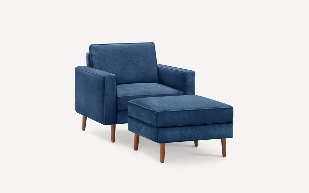 Modern navy blue upholstered armchair with matching cushioned ottoman, both featuring wooden tapered legs.