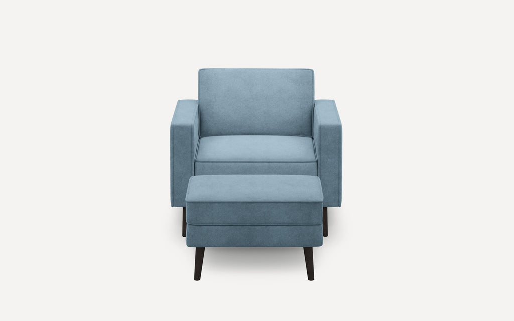 Modern blue upholstered armchair with matching ottoman, featuring clean lines and dark wooden tapered legs, shown on white background.