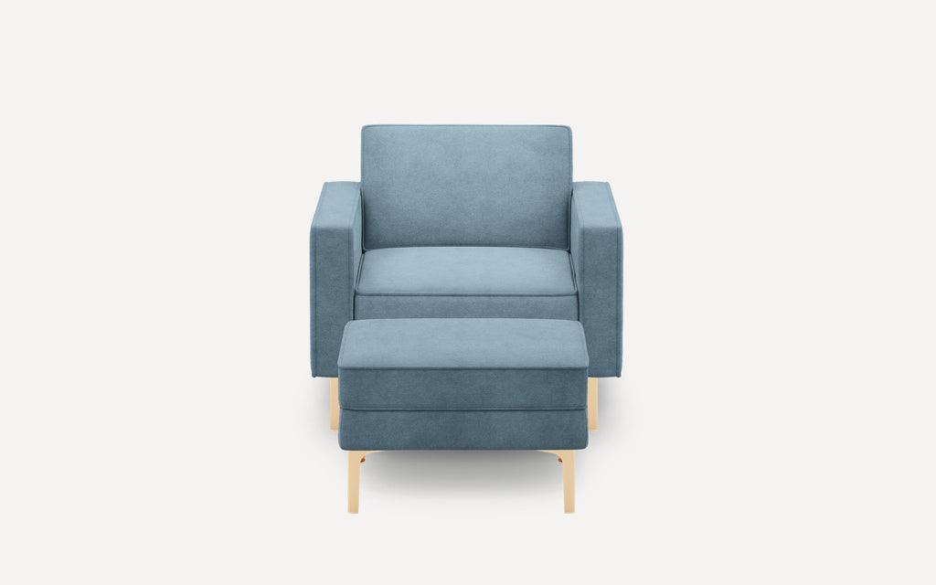 Modern light blue upholstered armchair with matching ottoman and gold metal legs, shown from front on white background.