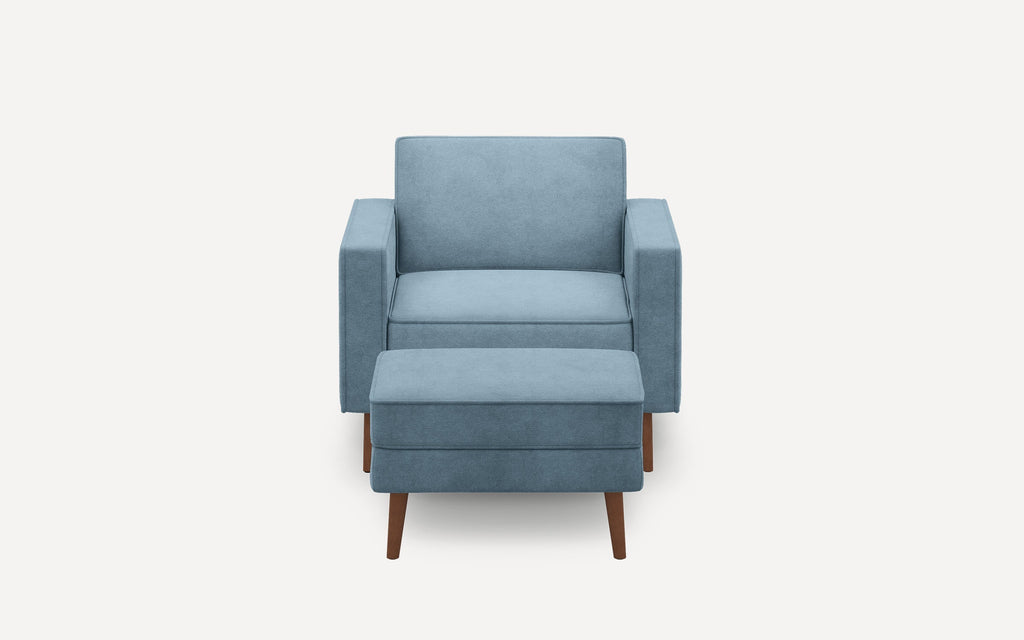 Front view of a modern blue upholstered armchair with matching ottoman and wooden tapered legs on a white background.