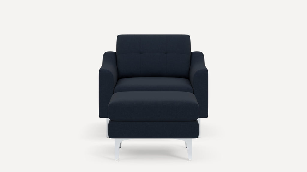 Modern navy blue upholstered armchair with matching ottoman and angled white metal legs on a plain background.