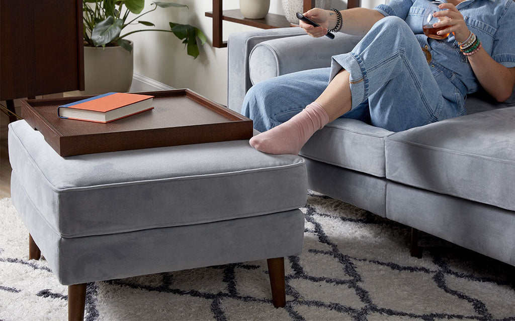 a woman sitting on a gray couch with a remote control device in her hand