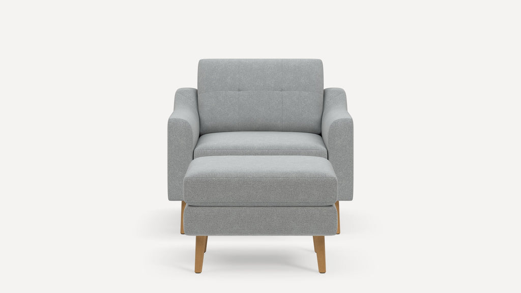 Front view of a modern light gray upholstered armchair with a matching ottoman and wooden legs on a white background.