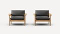 Two identical modern armchairs with light wood frames and dark gray cushions, set against a plain white background.