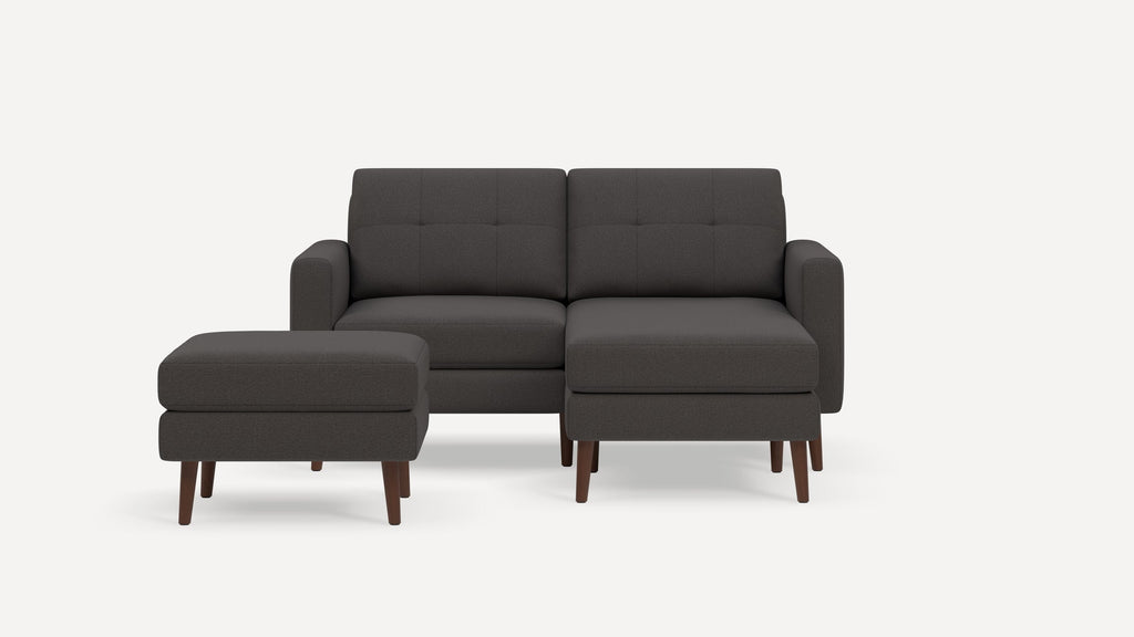 Dark gray fabric sectional sofa with wooden legs and matching ottoman on an off-white background.
