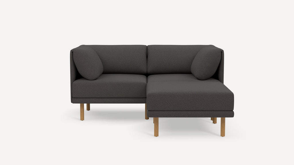 Modern dark gray fabric sectional sofa with wooden legs, featuring a chaise lounge on the right side and two round cushions.