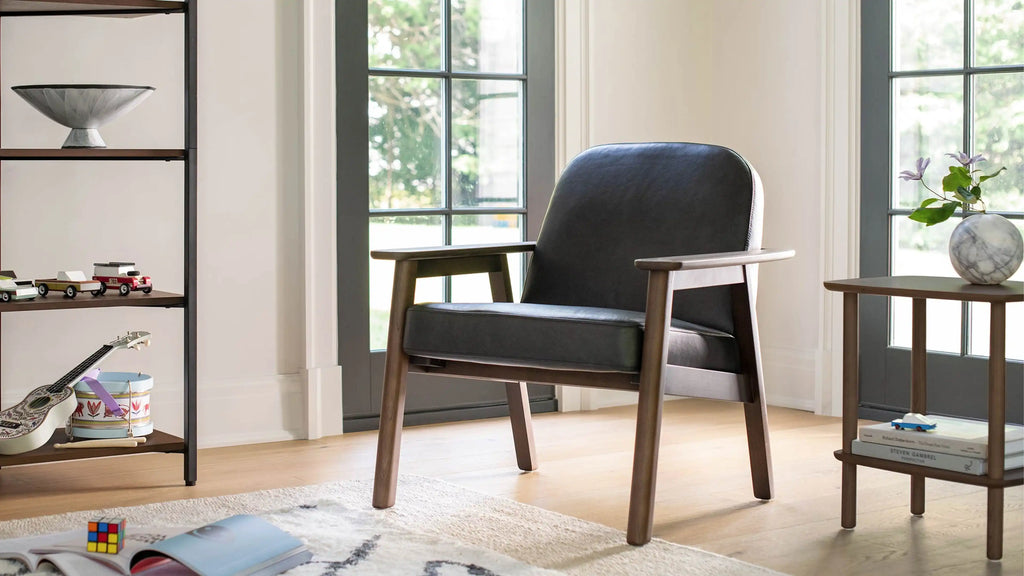 Modern black leather armchair with wooden frame in a bright room, next to a shelf with toys and a side table with vase.