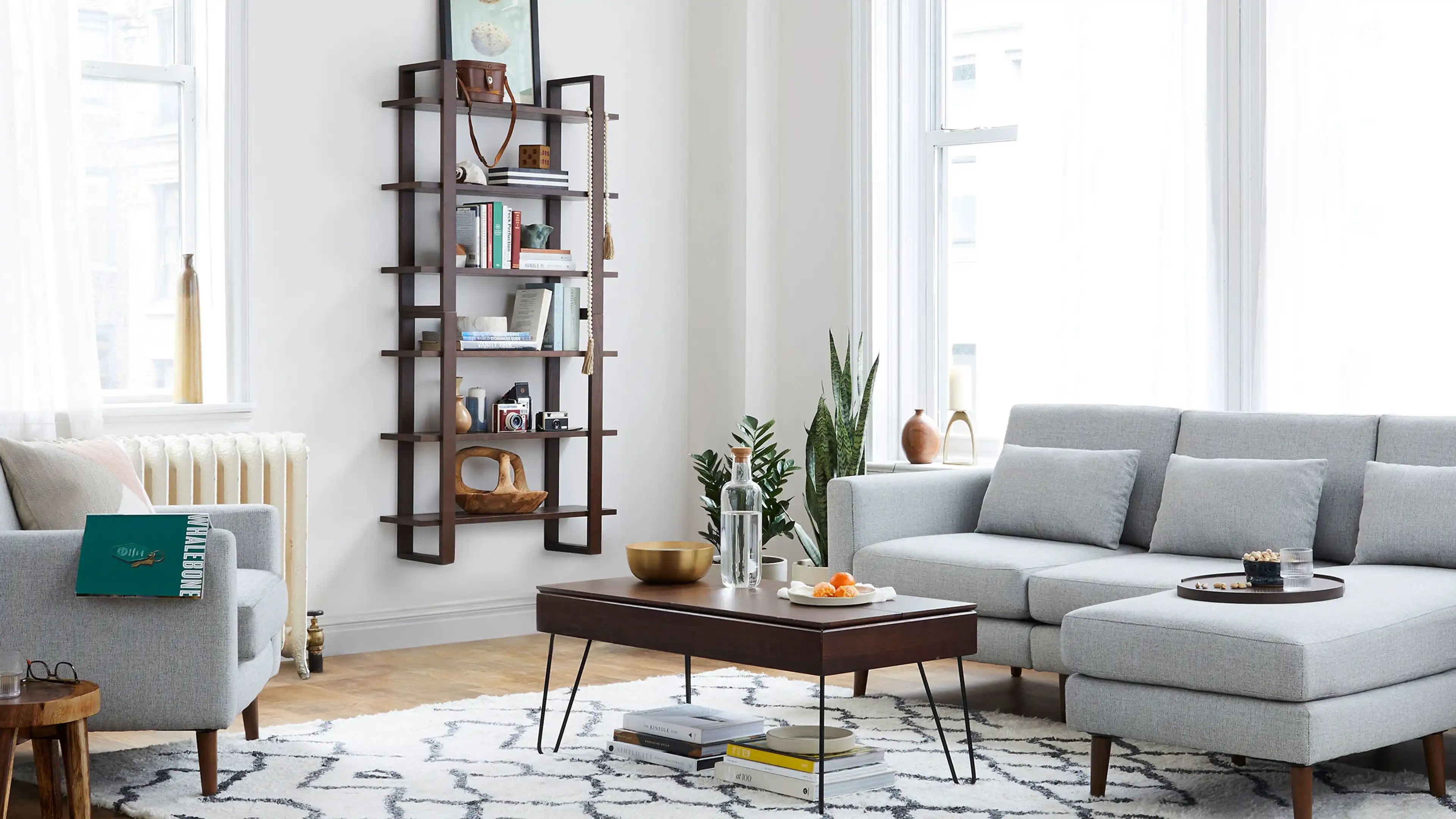 Modern living room with gray sectional sofa, wooden coffee table, wall-mounted bookshelf, and patterned area rug.