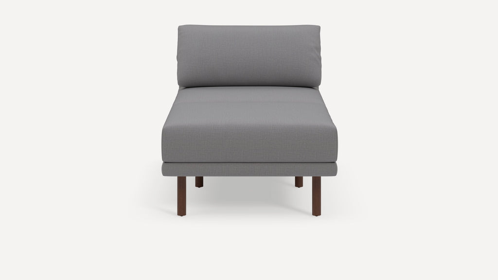 Front view of a modern, minimalistic gray upholstered armless lounge chair with dark wood legs on a white background.