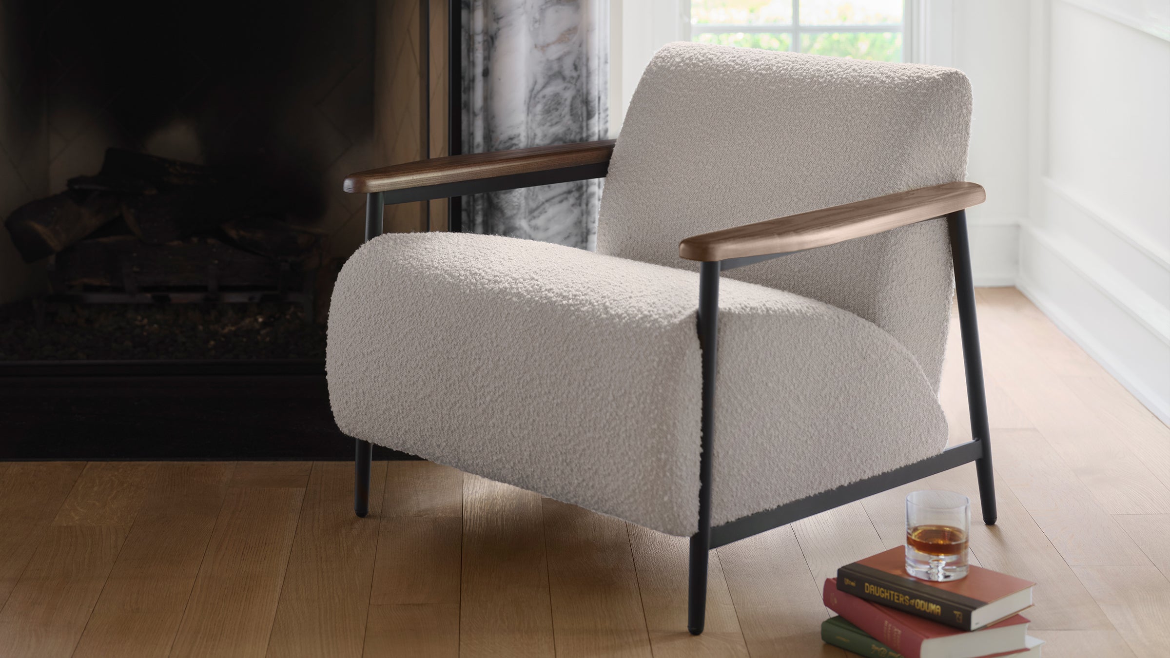 Modern armchair with textured light beige upholstery, wooden armrests, and black metal legs, situated near a fireplace on wooden flooring.