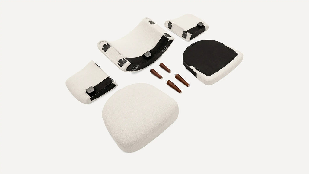 Disassembled white cushioned chair parts and four wooden tapered legs arranged on a plain background.