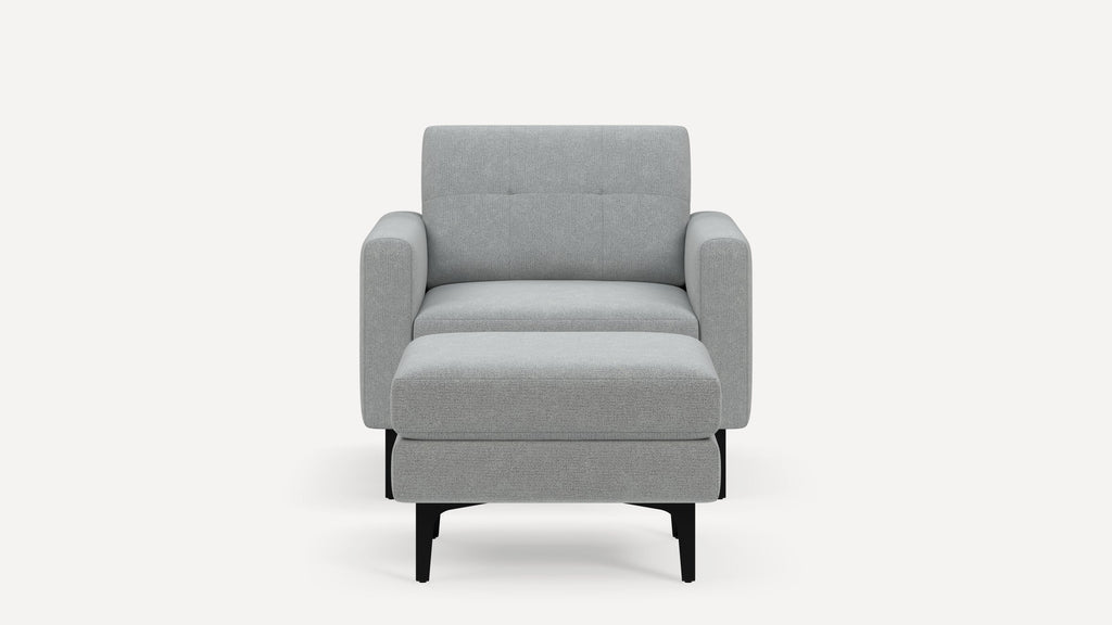 Front view of a modern, light gray upholstered armchair with a matching ottoman and black legs.