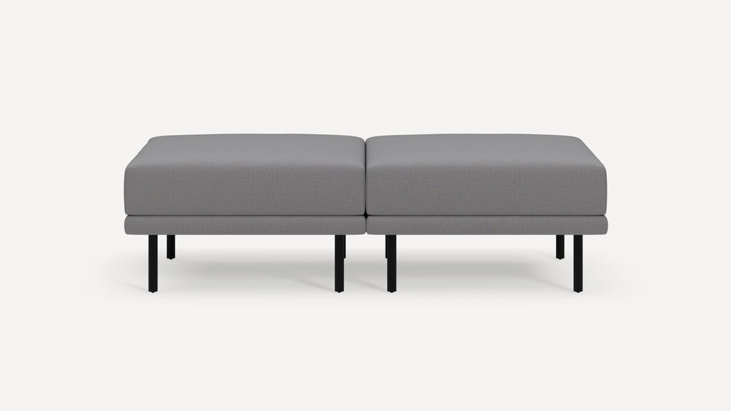 Modern gray fabric ottoman with black metal legs, consisting of two cushioned square sections placed side by side.