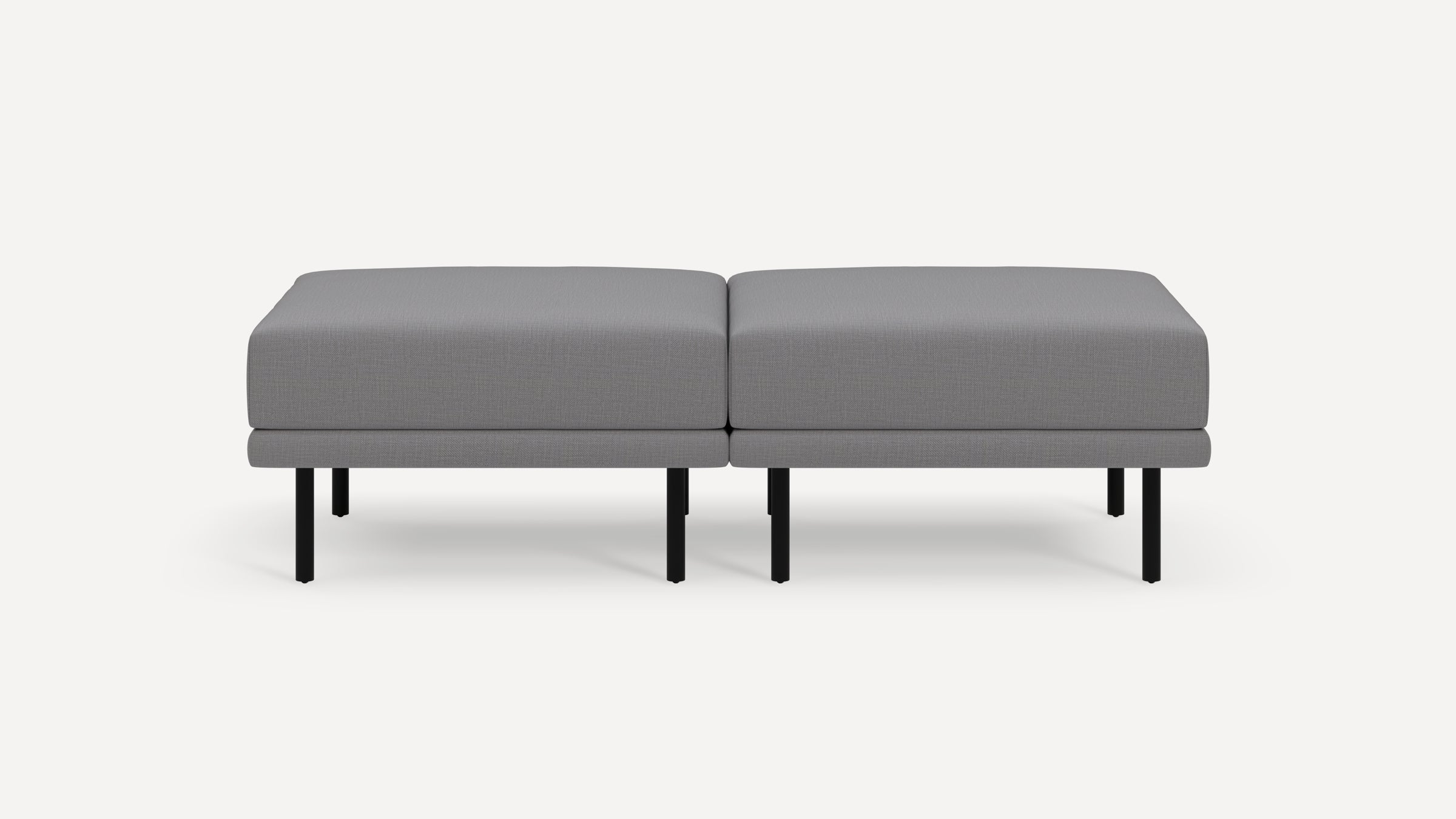 Modern gray fabric ottoman with black metal legs, consisting of two cushioned square sections placed side by side.