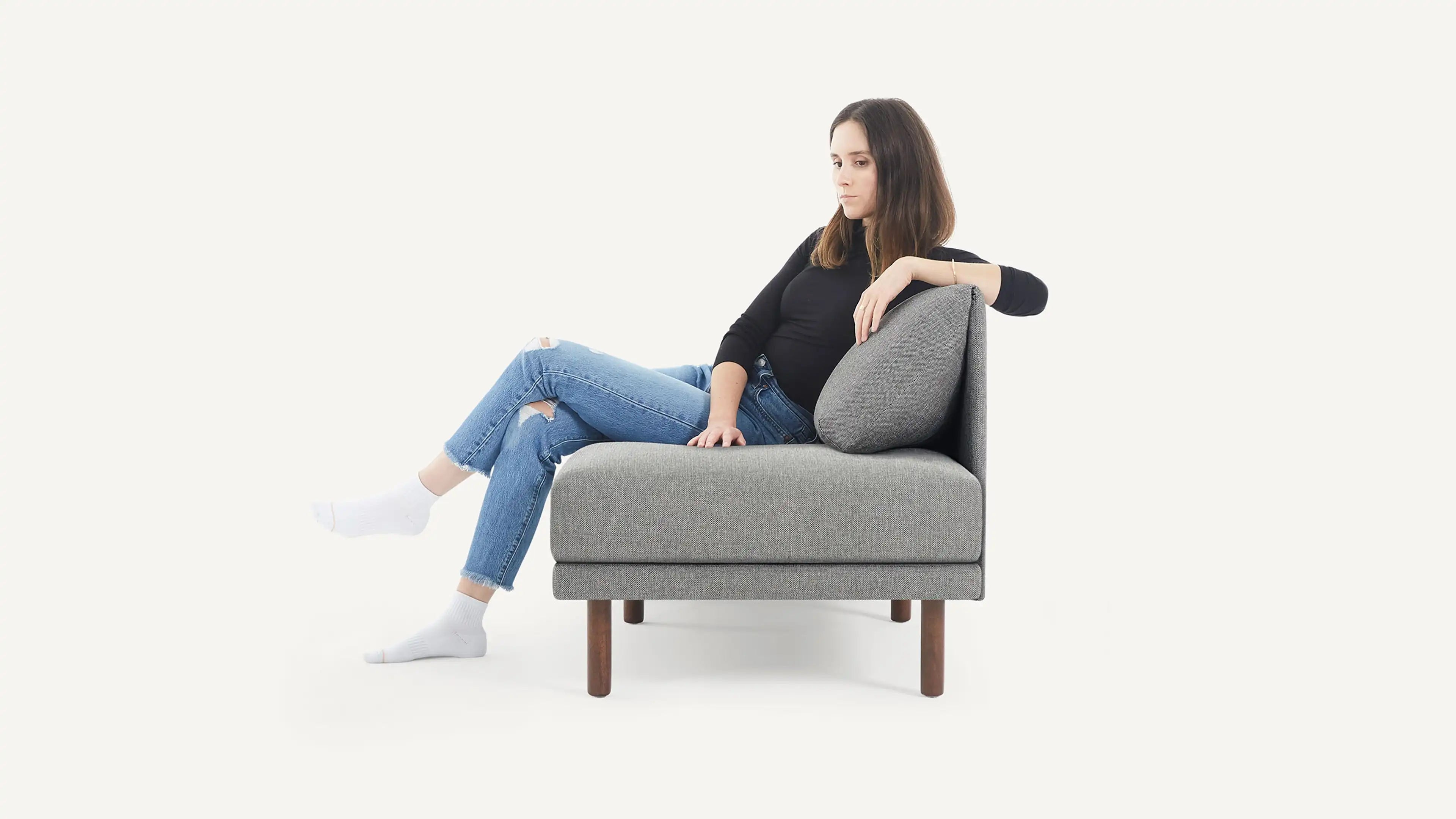 a woman sitting on a gray couch with her legs crossed, wearing white socks and a black top, black shirt, and white socks