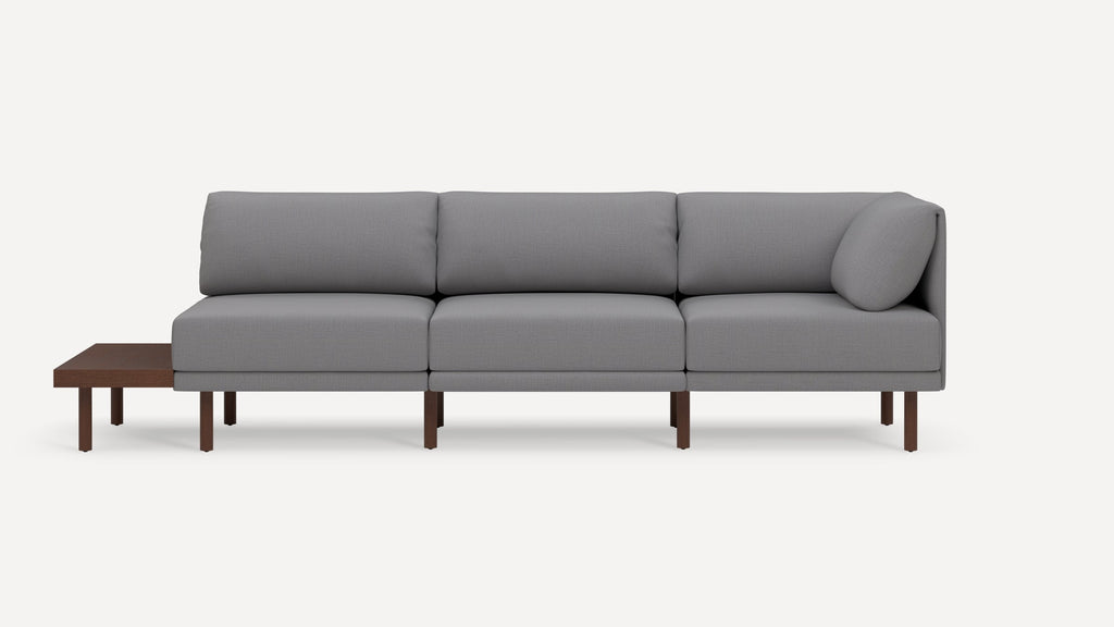 Modern sectional sofa with gray fabric upholstery, wooden legs, and an attached side table on the left end.