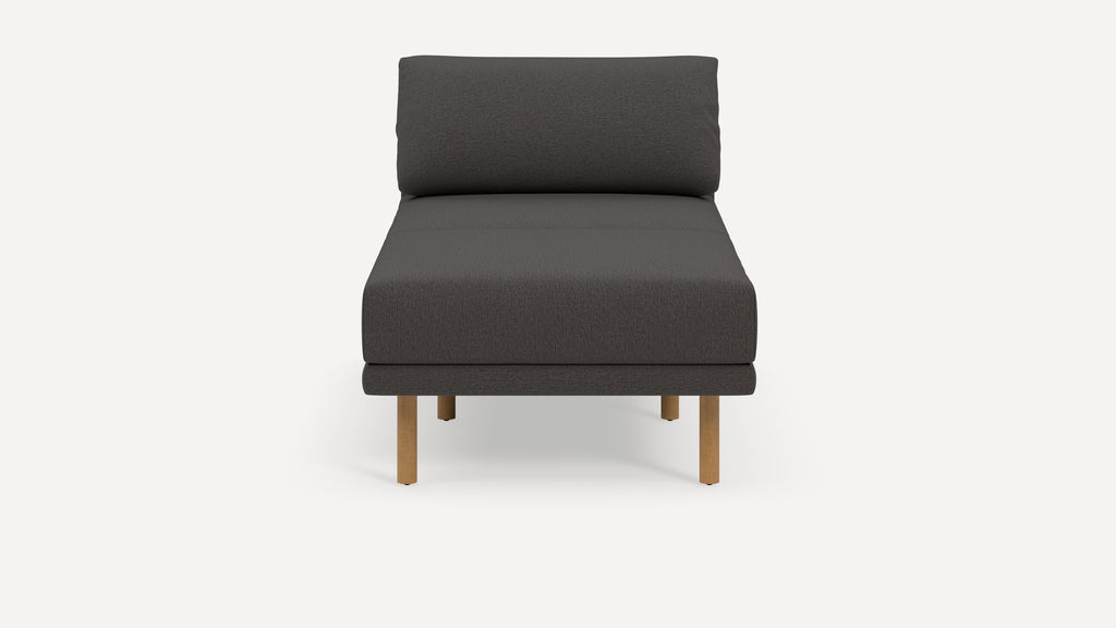 Front view of a modern dark gray upholstered armless lounge chair with light wooden legs on a white background.
