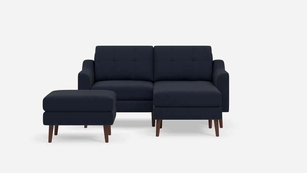 Dark blue fabric two-seater sofa with tufted back cushions and matching ottoman, featuring wooden legs on a white background.