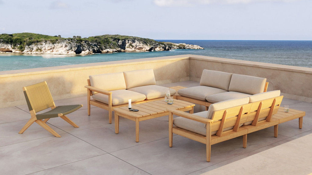 Outdoor patio set with light wood frames and beige cushions, includes sectional sofas, chair, and coffee table overlooking ocean view.