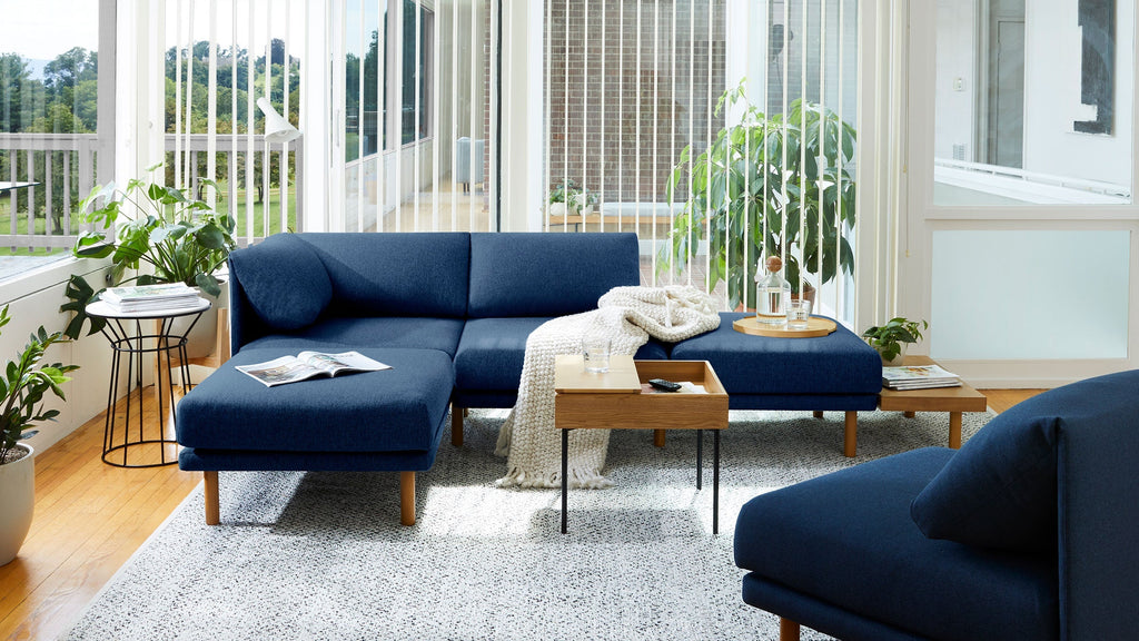 a living room with a blue couch, wooden coffee table, and plant pots on the floor