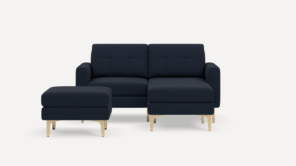 Modern navy blue sectional sofa with plush cushions, tufted backrest, and matching ottoman on sleek gold metal legs.