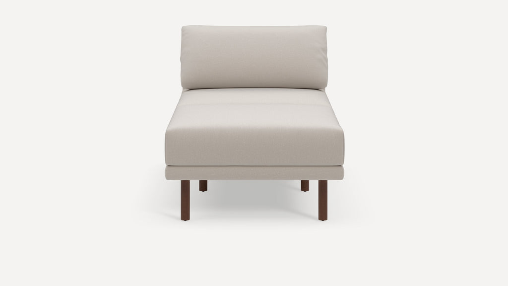Beige cushioned chaise lounge with a simple, modern design and four dark wooden legs on a plain white background.