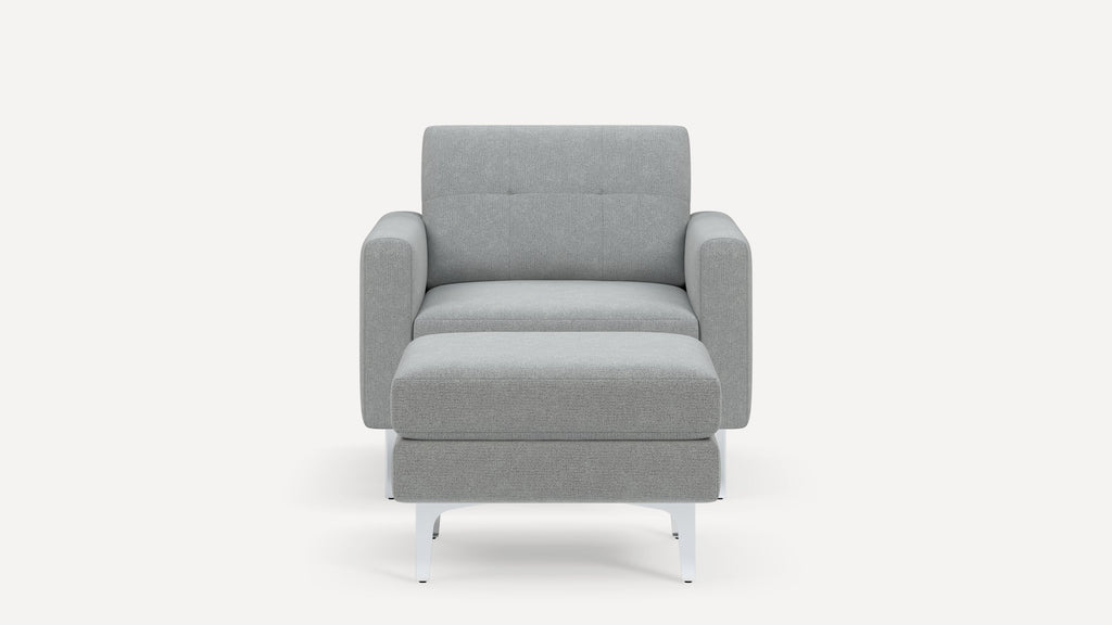 Front view of a modern gray upholstered armchair with thick cushions and white metal legs on a white background.