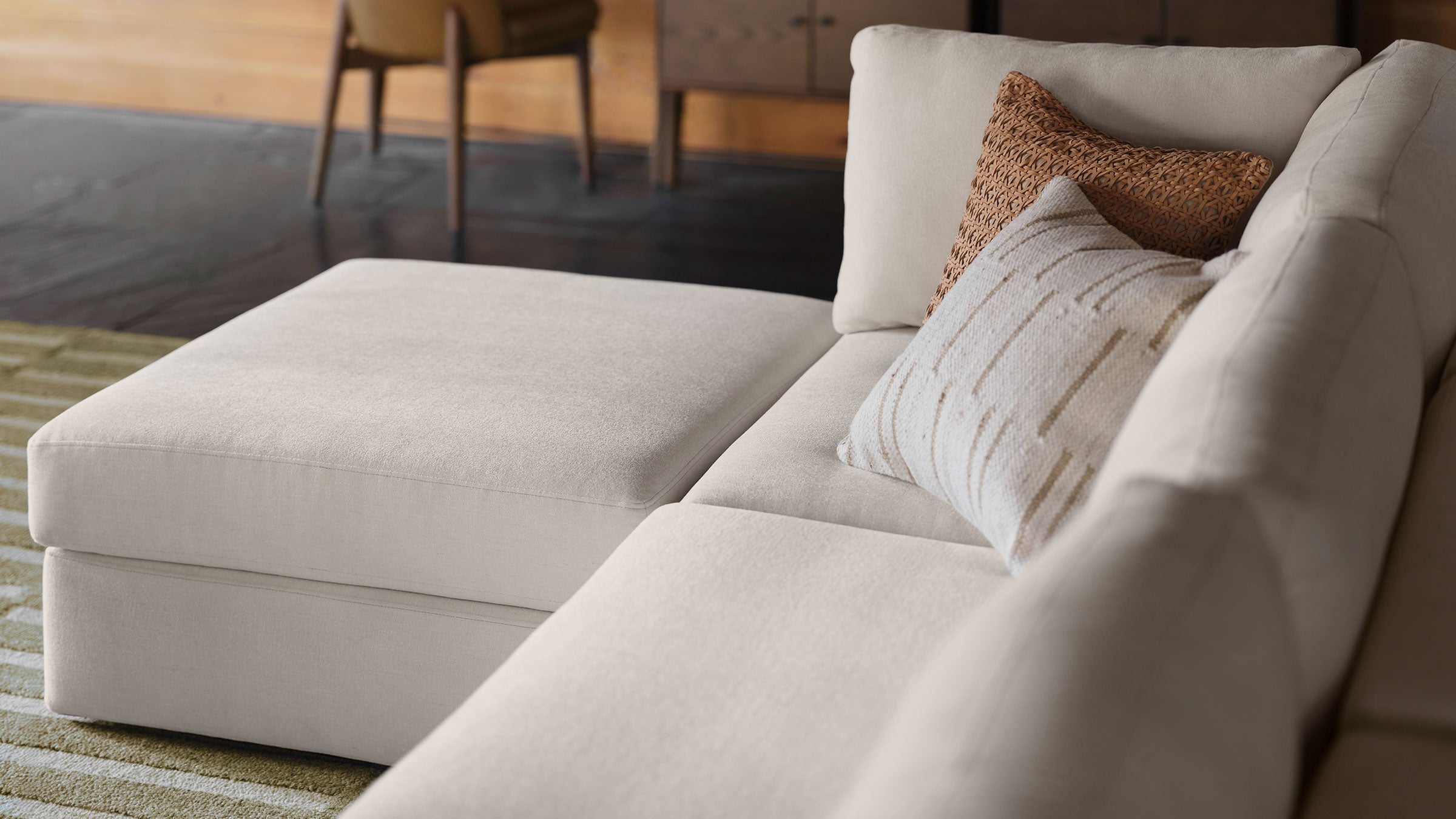 a beige sectional sofa with a matching ottoman and a decorative pillow on the back of the sofa