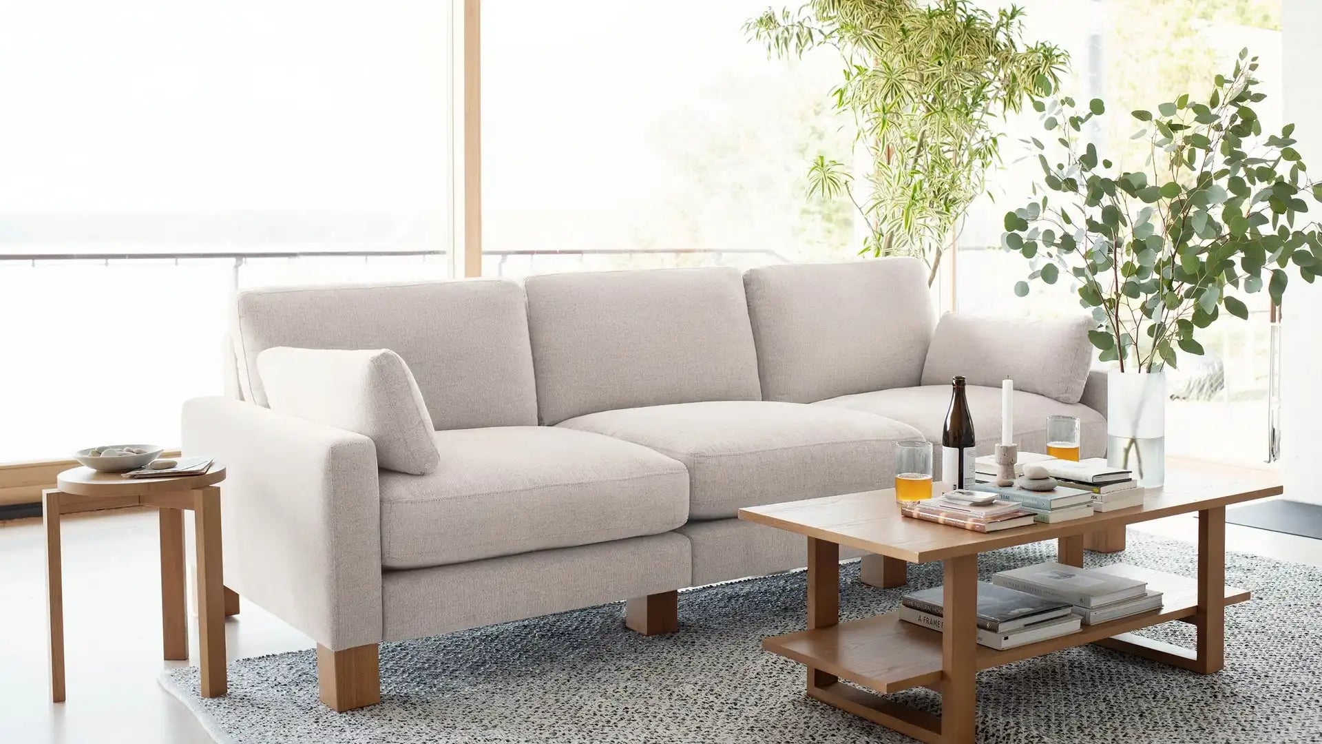 modern beige fabric sectional sofa with wooden legs and clean lines on a patterned rug in a living room with a large window