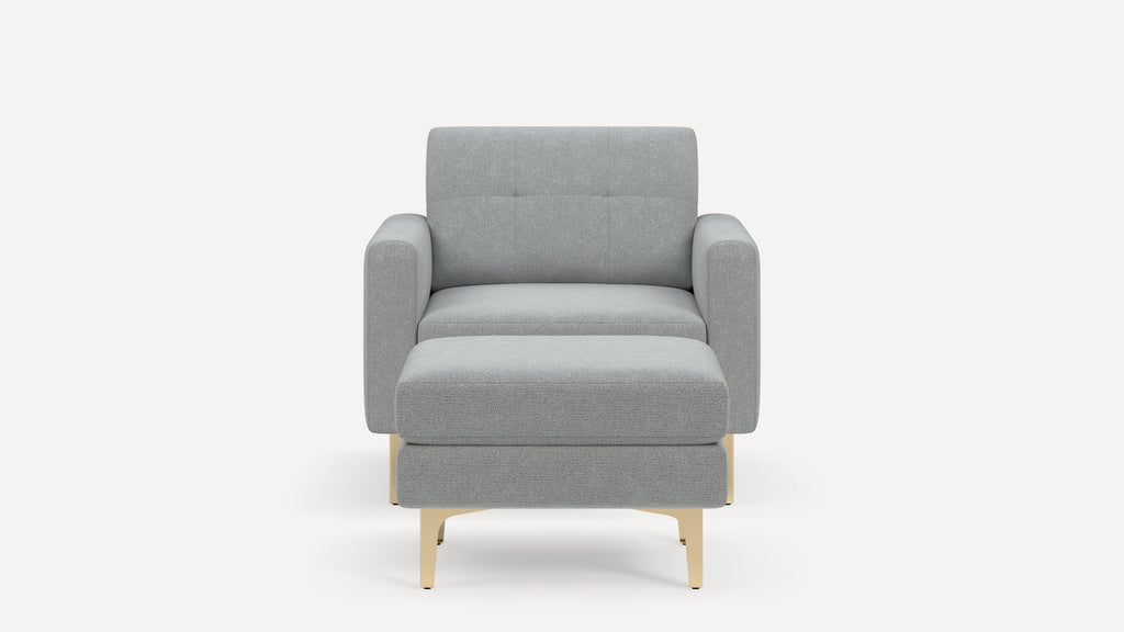 Front view of a modern light gray upholstered armchair with matching ottoman and beige legs on a white background.
