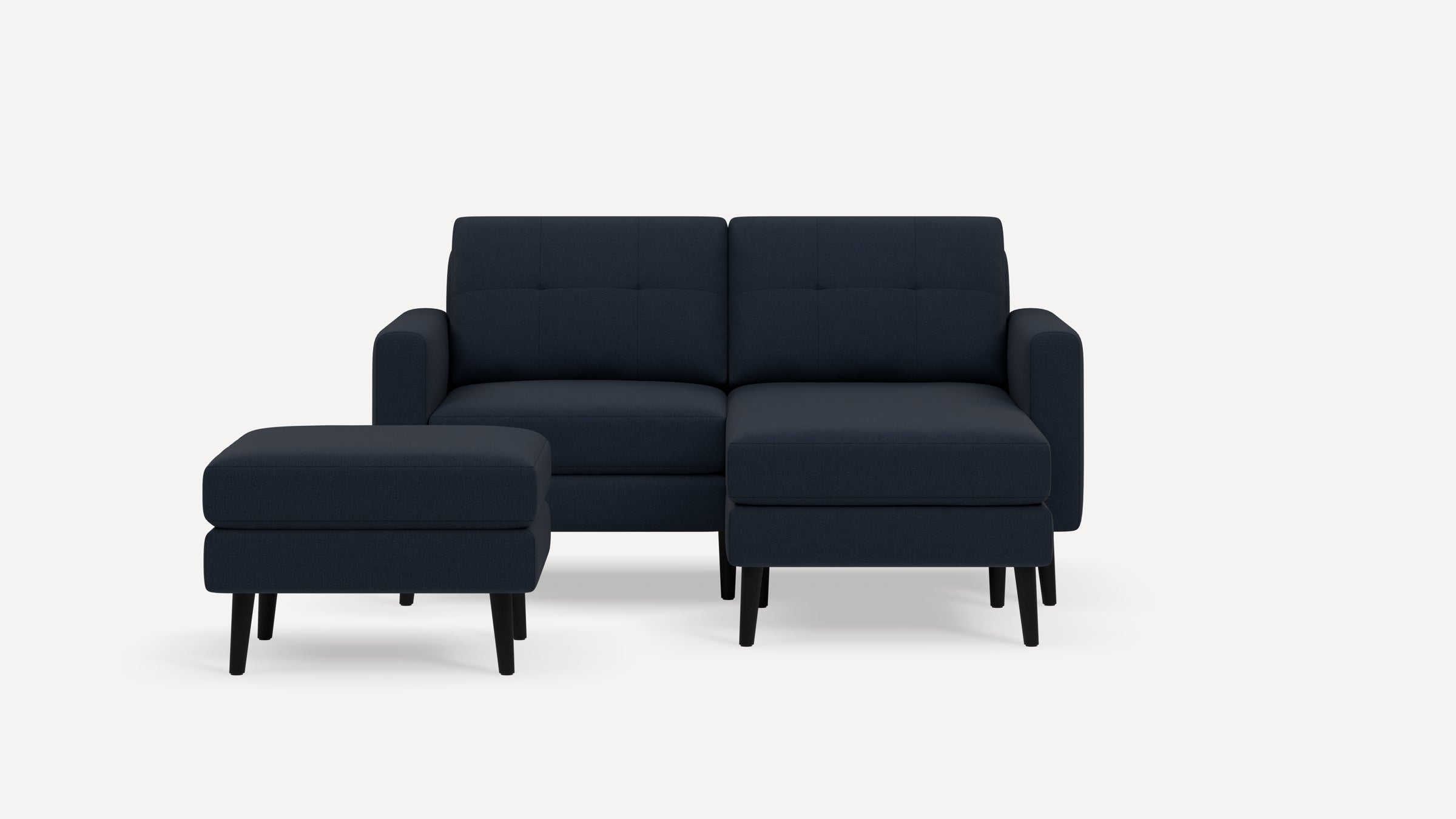 Modern dark blue fabric sectional sofa with left armrest and matching ottoman, featuring tufted back cushions and black wooden legs.