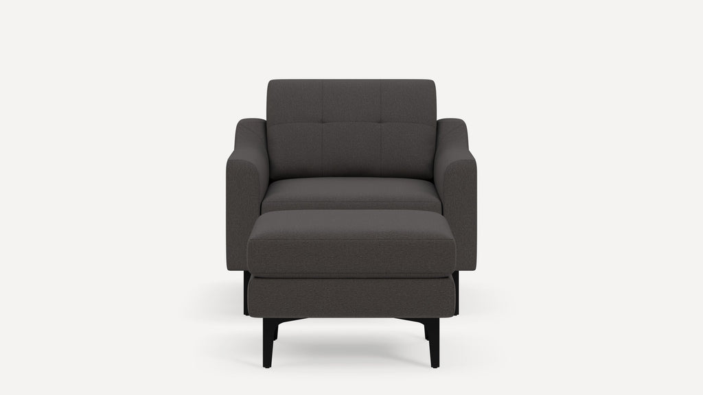 Front view of a modern dark gray upholstered armchair with matching ottoman on black legs against white background.
