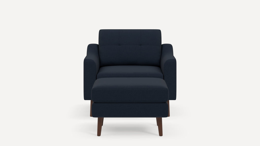 Front view of a modern navy blue armchair with matching ottoman and tapered wooden legs on white background.