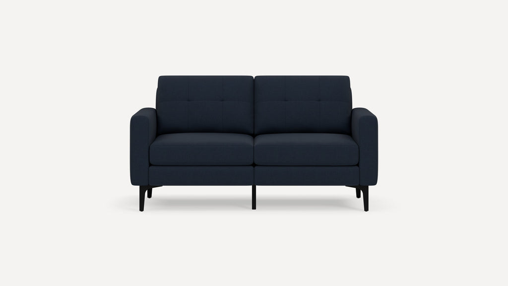 Modern navy blue two-seater sofa with tufted back cushions, plush seat cushions, rounded armrests, and slender black legs on white background.