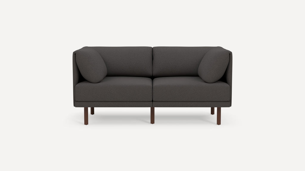 Modern dark gray two-seater sofa with rounded armrests and cushions, elevated on wooden legs, against a plain white background.