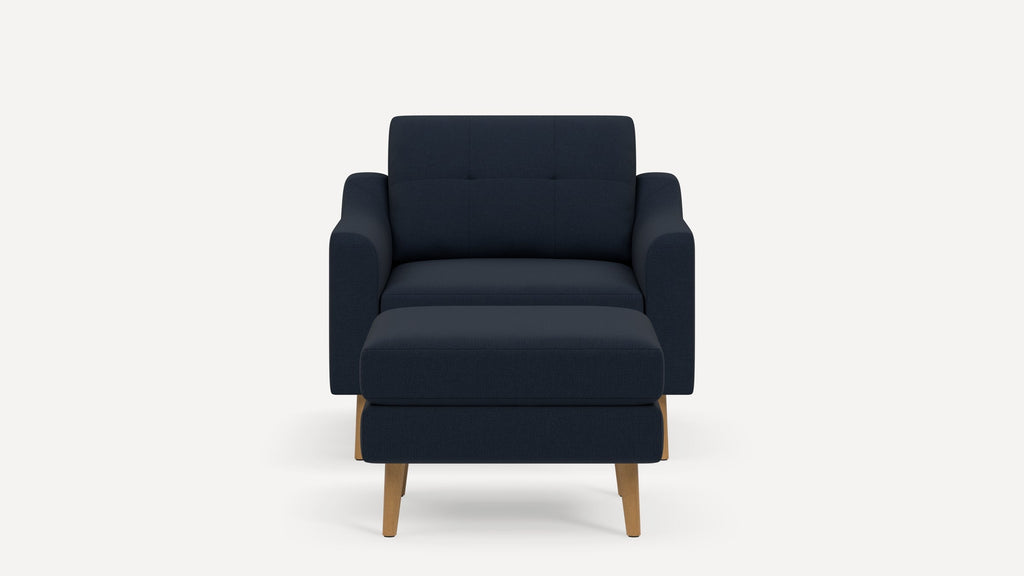Modern navy blue fabric armchair with matching ottoman, featuring wooden legs and a tufted backrest against a white background.