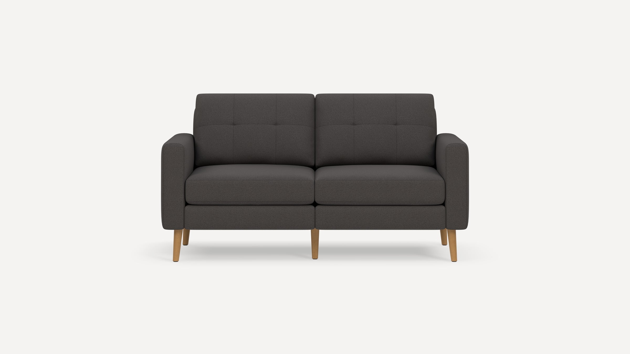 Mid-century modern dark gray upholstered two-seater sofa with tufted back cushions and light wooden legs on white background.