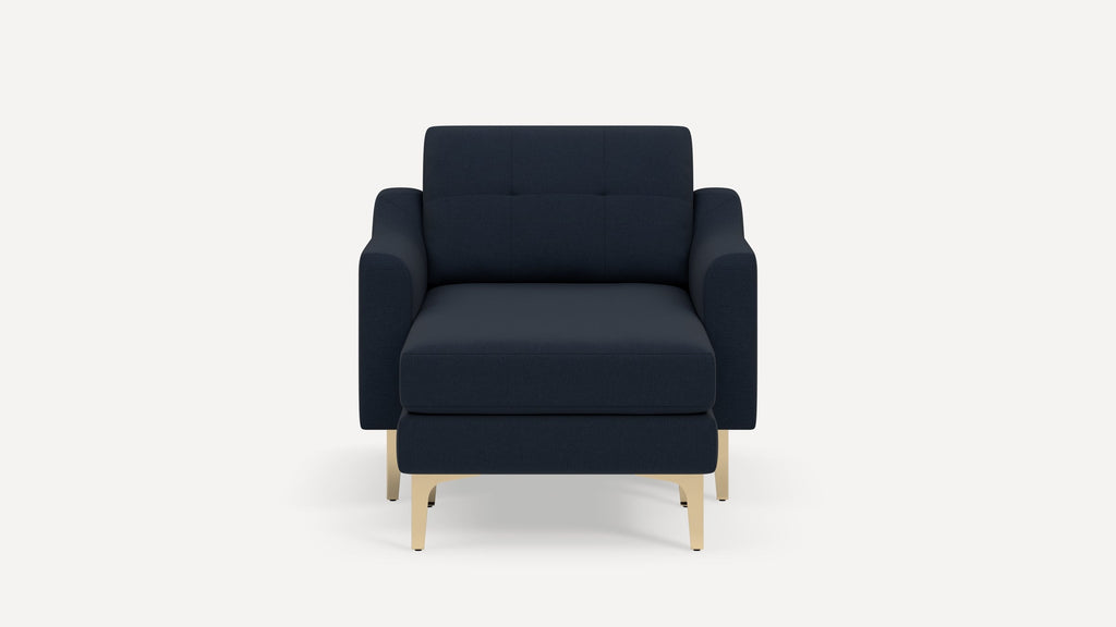 Front view of a modern navy blue armchair with a matching ottoman and light wooden legs on a white background.