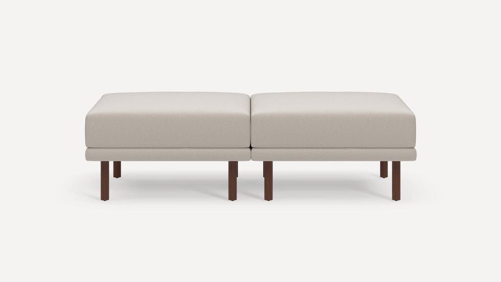 Two beige cushioned ottomans with simple rectangular shape, supported by dark wooden legs, placed side by side.