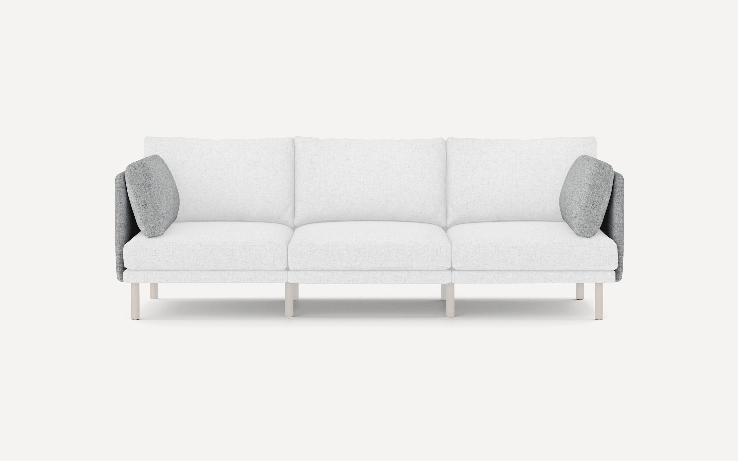 Modern three-seater sofa with white cushions, light wooden legs, and contrasting grey side pillows, minimalist design.