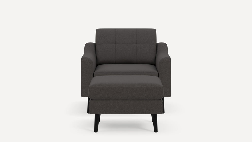Front view of a modern dark gray upholstered armchair with a matching cushioned ottoman and black wooden legs.