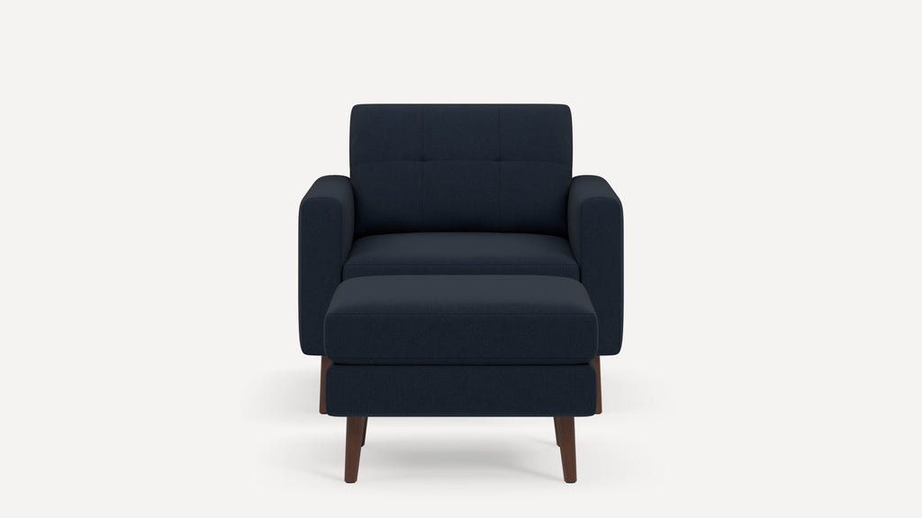 Front view of a modern navy blue armchair with matching ottoman, wooden legs, and padded cushions.