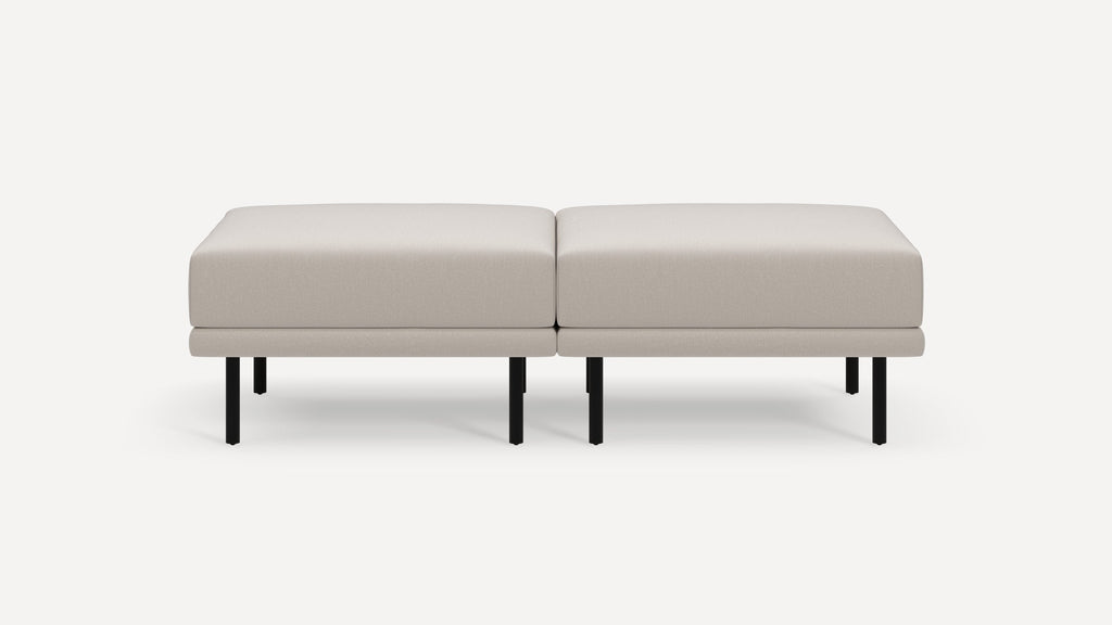 Modern beige upholstered bench with clean lines, two cushions, and black metal legs on a white background.