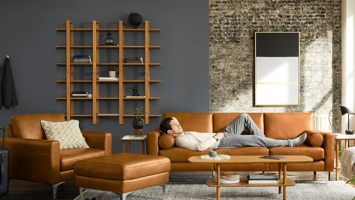 Modern living room with tan leather sofa set, matching ottoman, wooden coffee table, and a man reclining on the sofa.